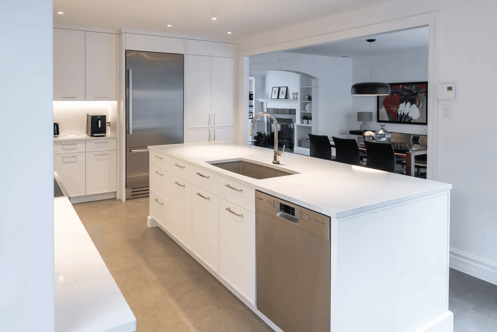 Modern white kitchen with large central island, integrated sink, stainless steel appliances, full-height cabinetry and an opening to a contemporary dining room.
