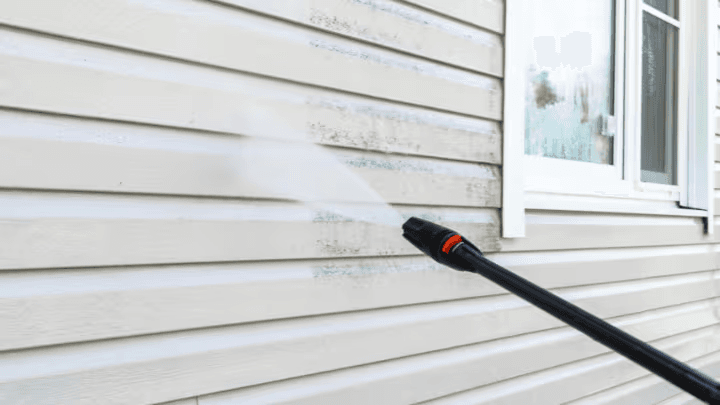 Pressure washing white exterior house siding to remove accumulated dirt, stains and surface buildup.