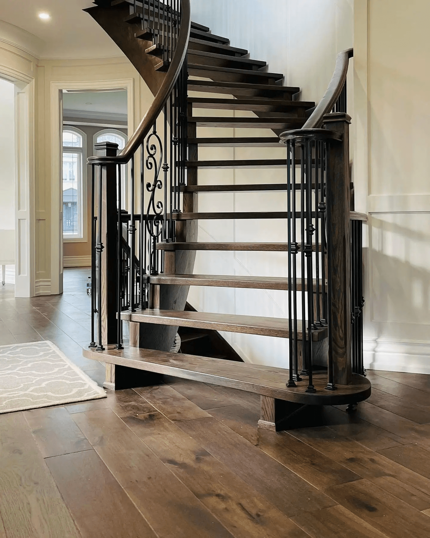 Curved wooden staircase with wrought-iron railing in an elegant interior with solid wood flooring and decorative wall mouldings.