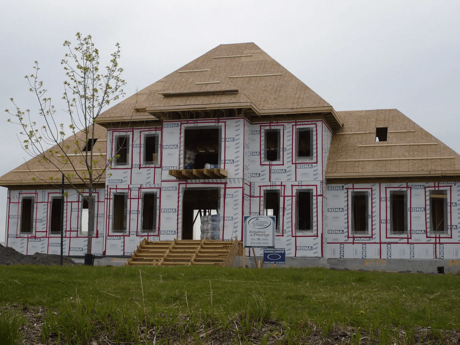Residential house under construction with roof framing, wood sheathing, air barrier membrane and window openings before exterior cladding installation