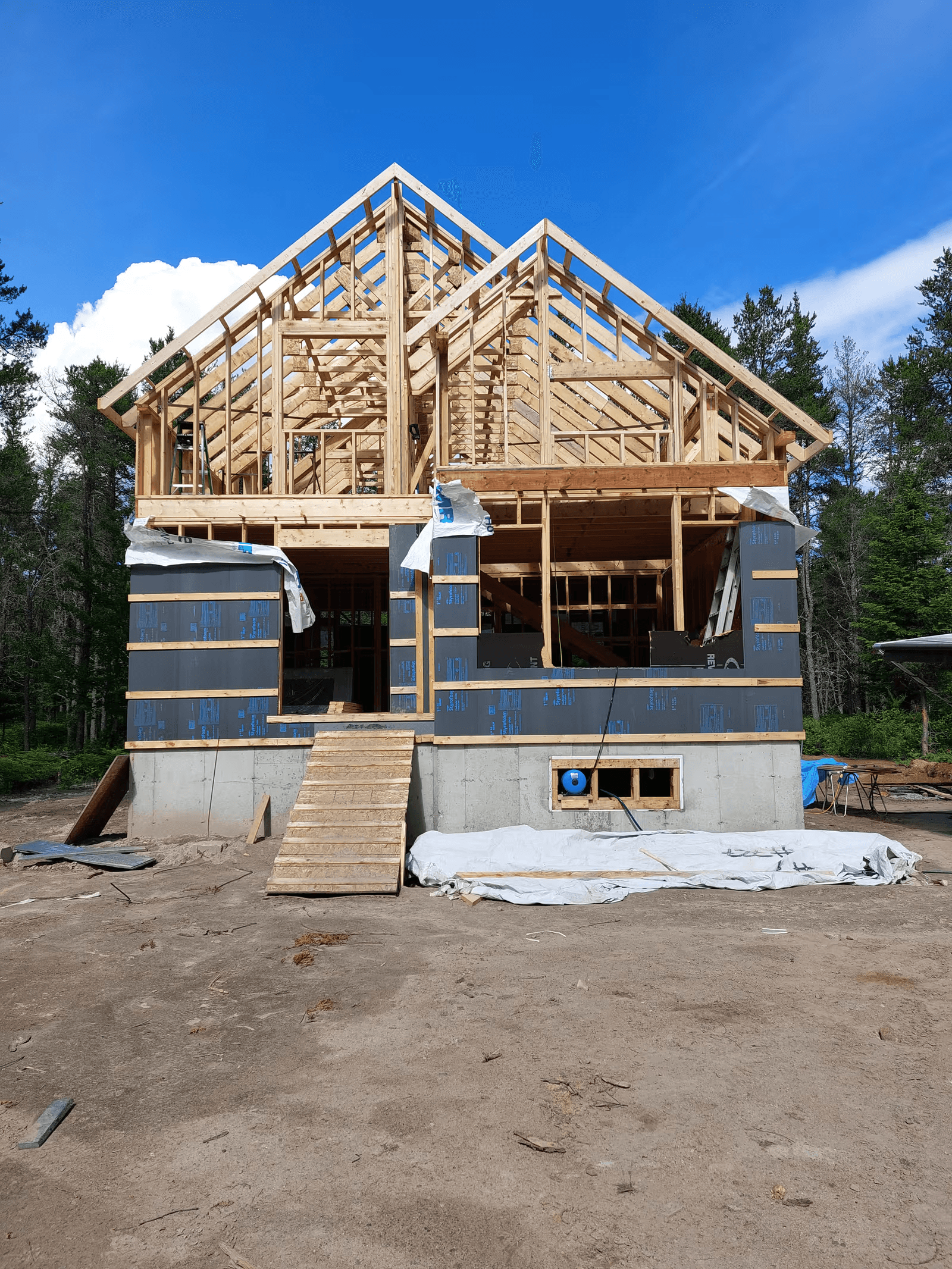 New home under construction with complete wood framing, exposed roof trusses, concrete foundation and partially installed exterior building envelope