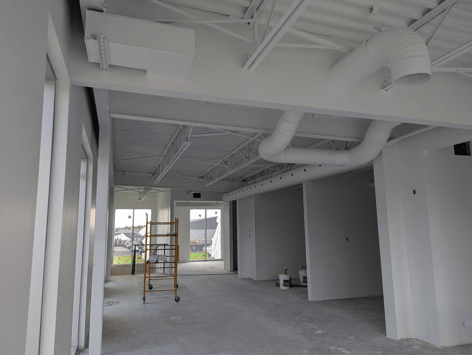 Commercial interior under renovation with an exposed white-painted ceiling, visible ventilation ducts, new partition walls and a mobile scaffold