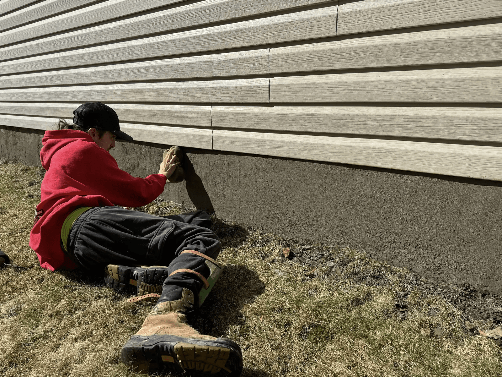 Worker hand-finishing freshly applied parging on the exterior foundation of a residential house.