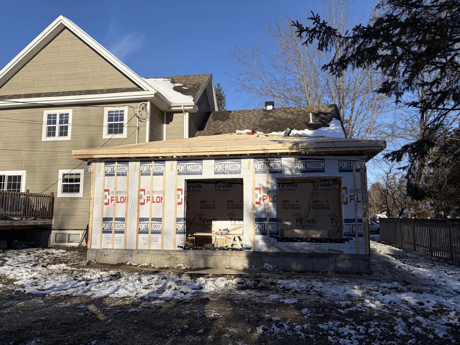 Residential home extension under construction with new roof framing, insulated walls, concrete foundation and window openings in winter.