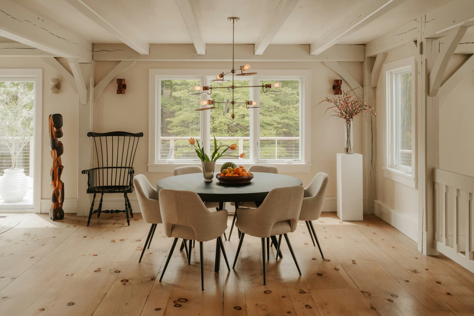 BrighBright, warm dining room with a round table, upholstered chairs, exposed beams, wood flooring and large windows overlooking naturet, warm dining room with a round table, upholstered chairs, exposed beams, wood flooring and large windows overlooking nature