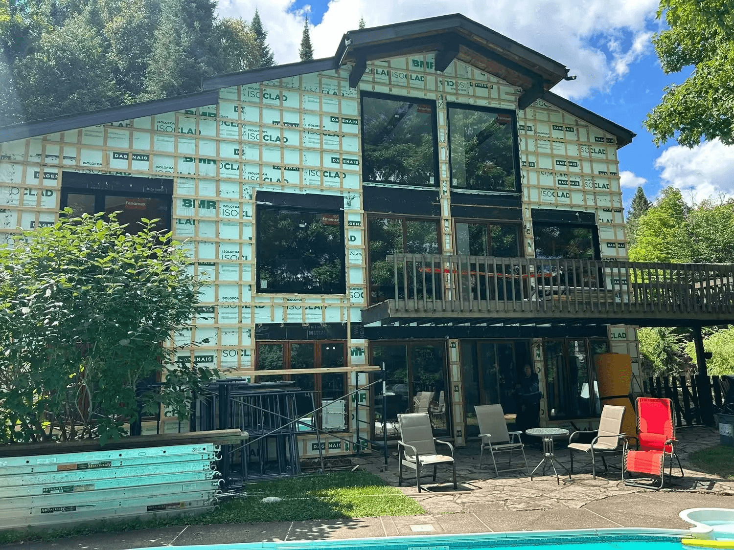 Residential home undergoing exterior renovation with rigid insulation panels, wood furring strips, large black windows and preparation for new siding
