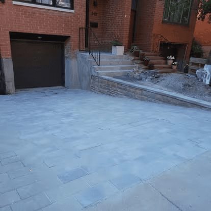 Grey interlocking paver driveway in front of a brick home with an integrated garage, retaining wall and exterior stone steps