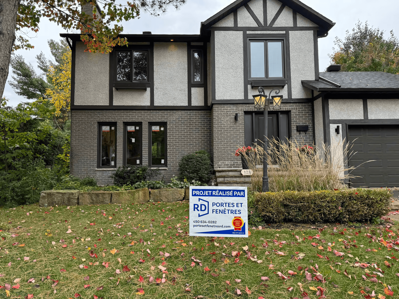 Renovated residential home exterior with new dark-framed windows, front door, garage, contrasting exterior finishes, and autumn landscaping.