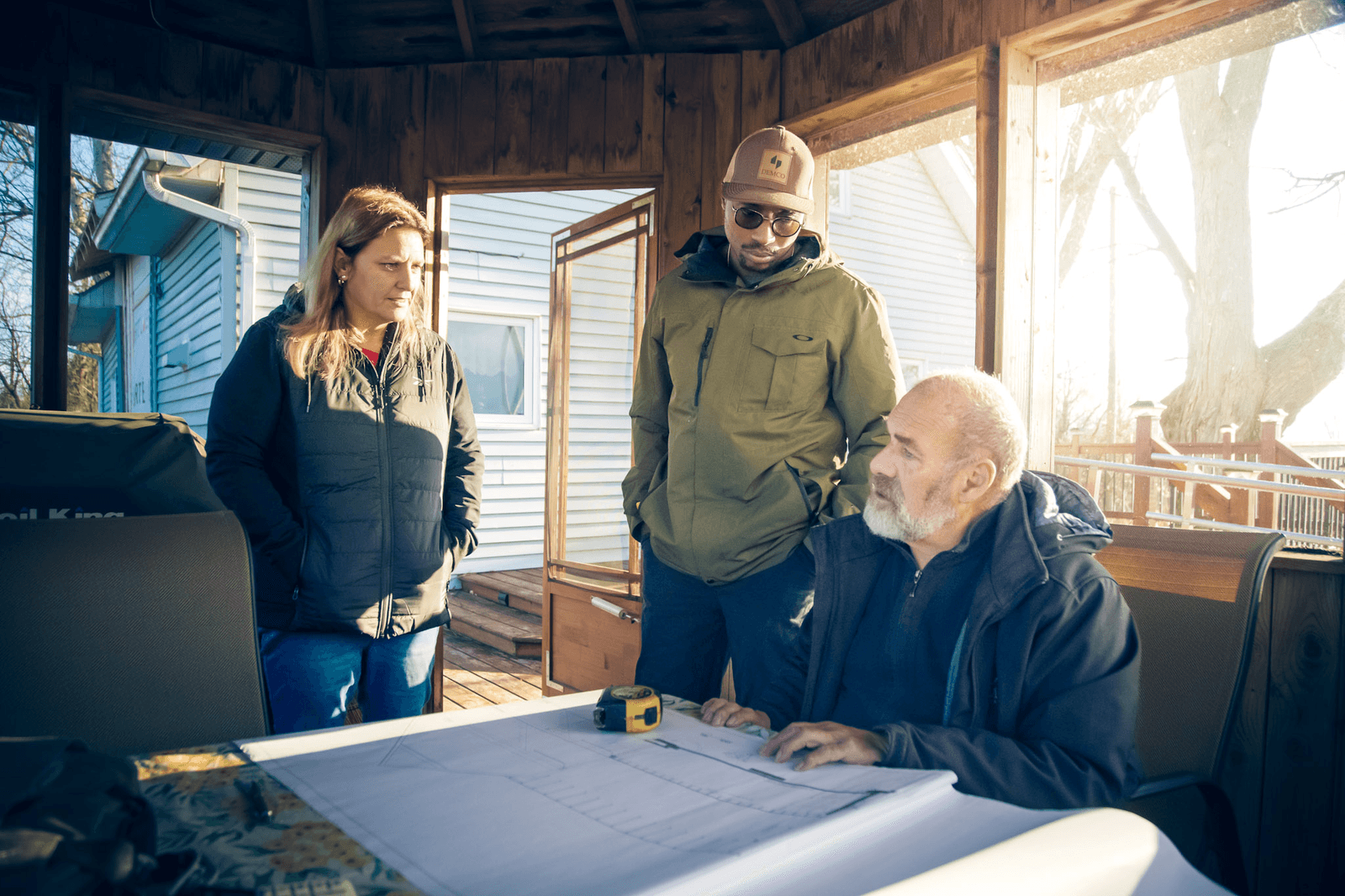 Meeting between a contractor and clients to review construction plans in a wooden sunroom.