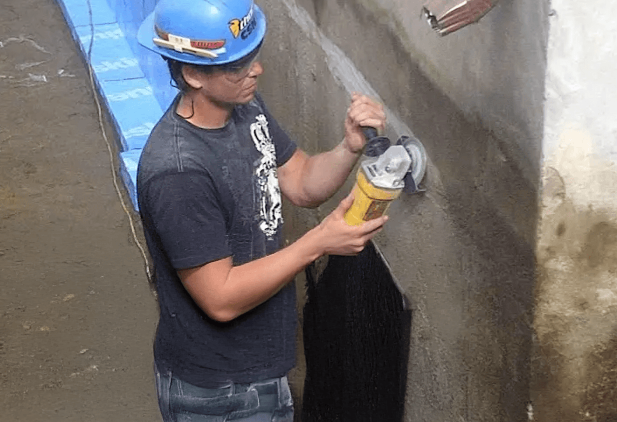 Worker grinding a concrete foundation in preparation for waterproofing.
