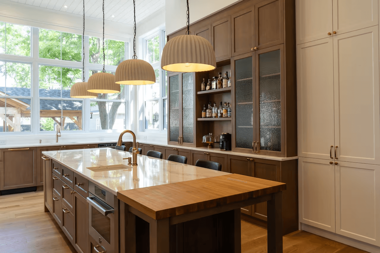 High-end kitchen with a large central island, wood and white cabinetry, light countertop, pendant lighting and expansive windows