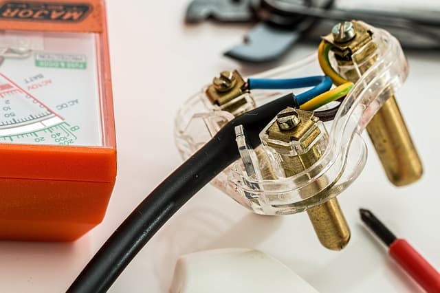 Close-up of electrical wires connected in a transparent terminal block with voltage tester, screwdriver and wiring tool.