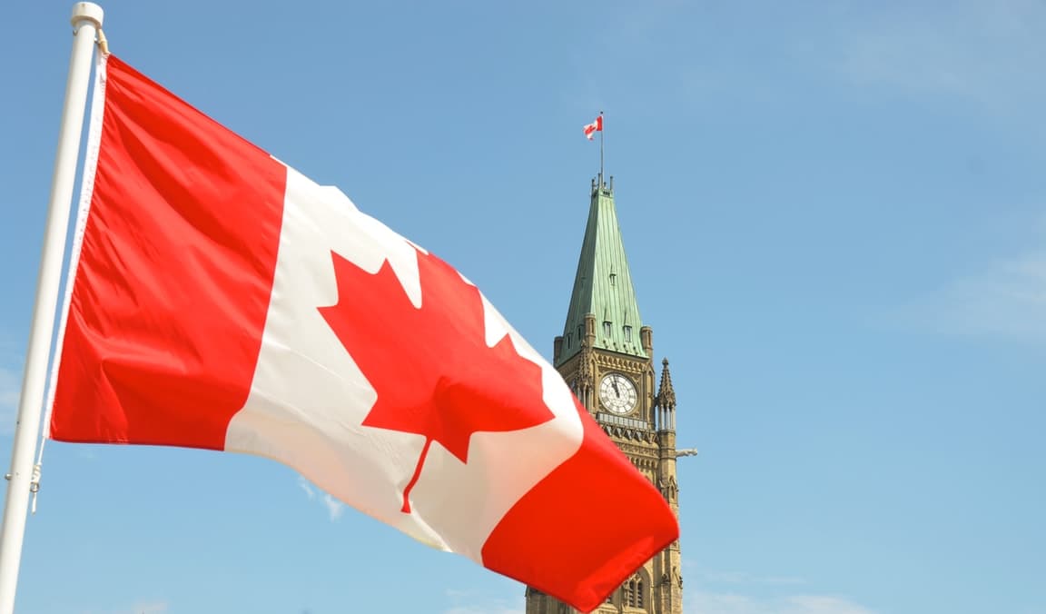 Canadian flag waving in front of the Peace Tower at Parliament Hill in Ottawa under a clear blue sky.