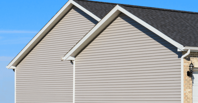 House gable with beige exterior siding, white soffits and black shingle roof.