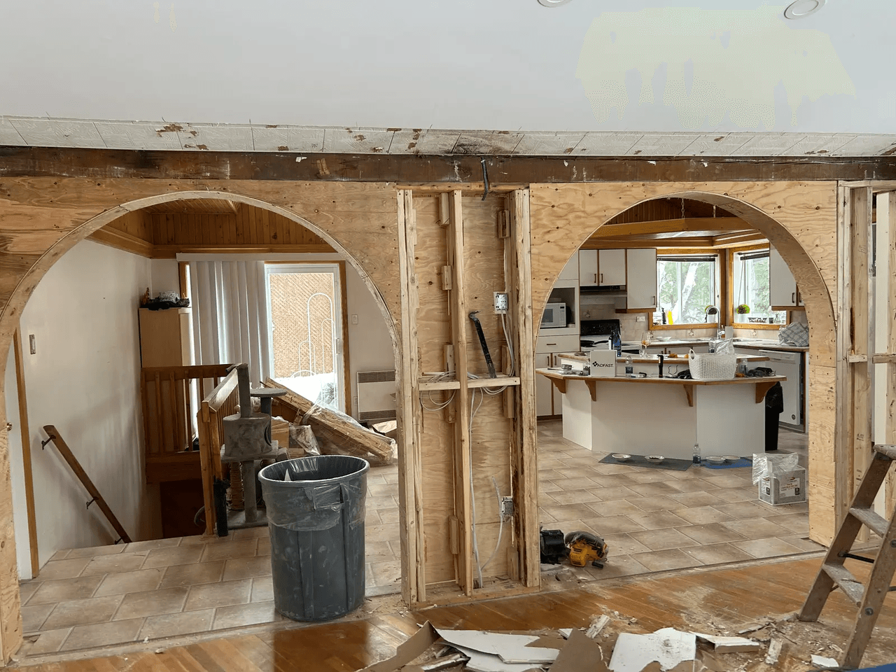 Interior renovation with open walls, wooden arches, exposed wiring and kitchen in background
