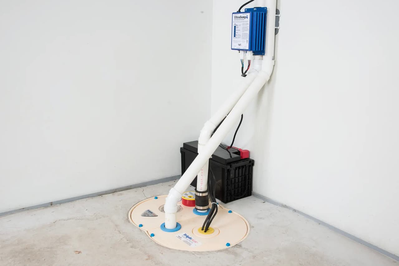Sump pump system with PVC pipes, backup battery and electrical control box installed in a basement.