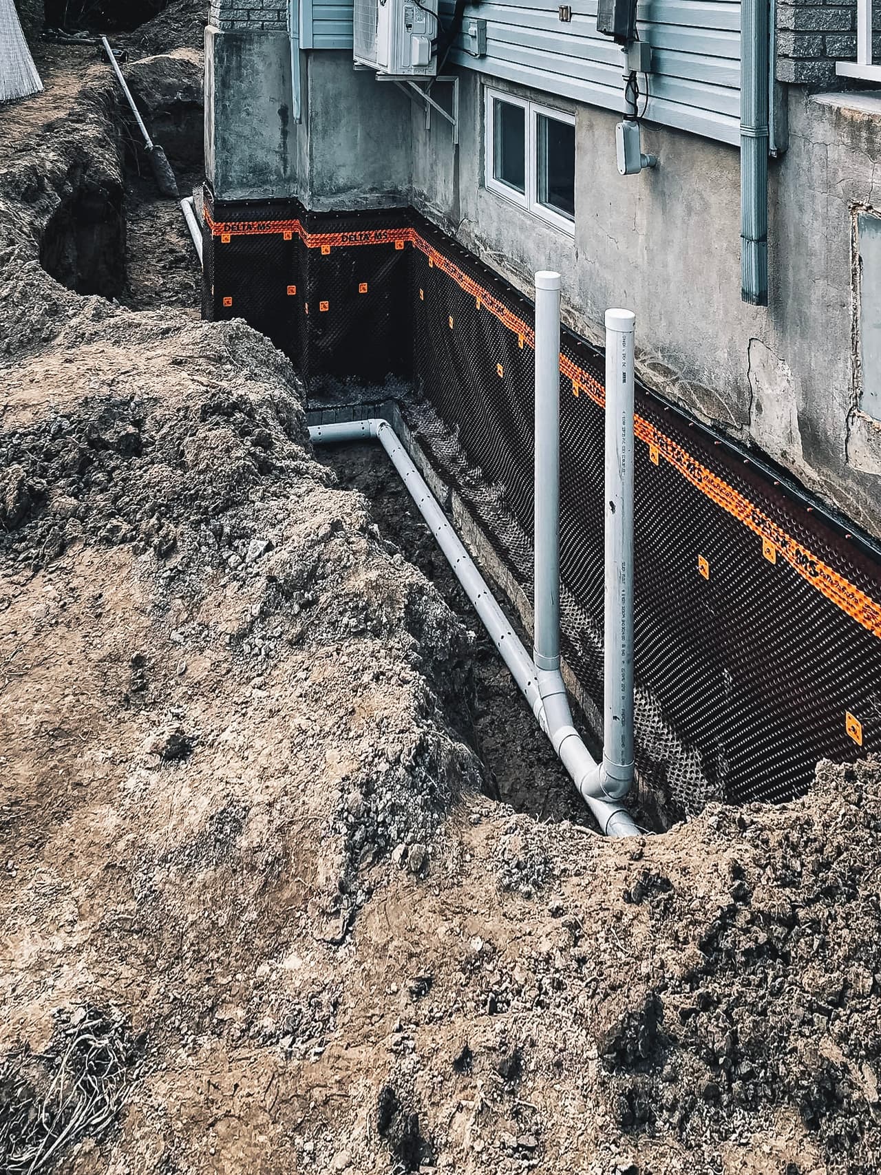 Excavation work for the installation of a French drain and waterproofing membrane on a house foundation.