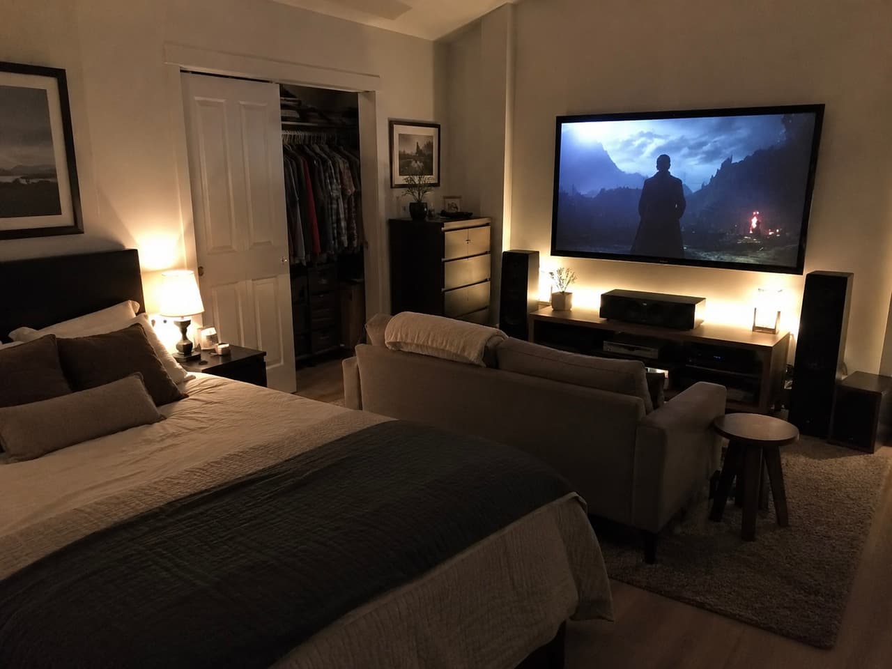 Bedroom featuring a home theater setup with a large wall-mounted TV, surround sound system, sofa and warm ambient lighting.