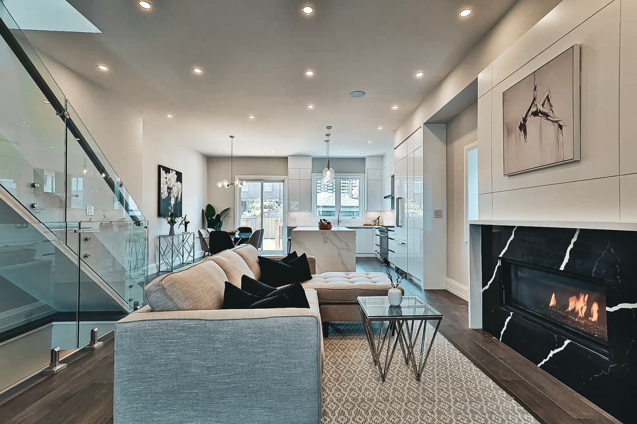 Modern living room with a black marble fireplace, glass staircase, and sleek open-concept kitchen