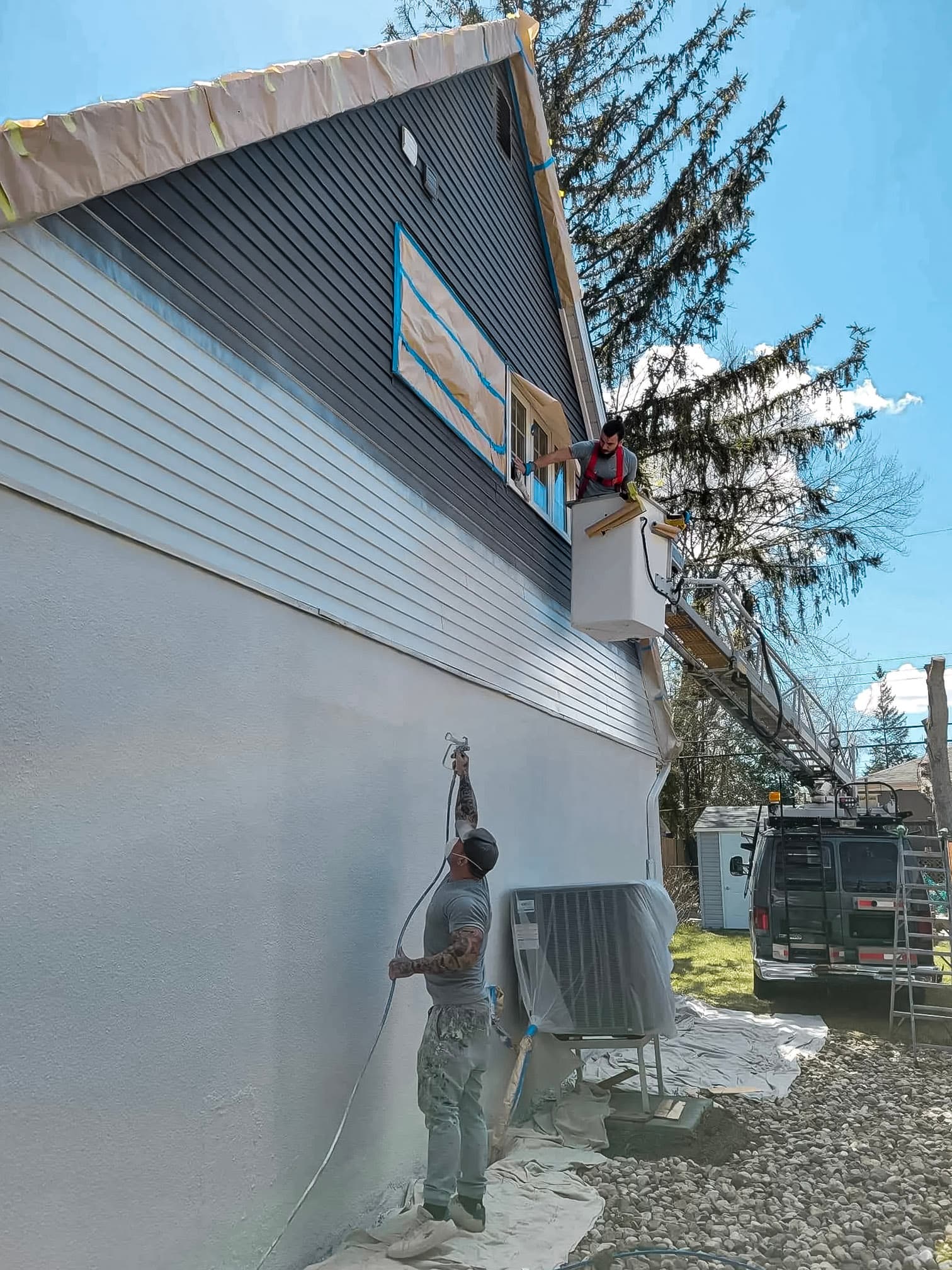 Exterior painting work being carried out on a house using a spray gun under a sunny sky.
