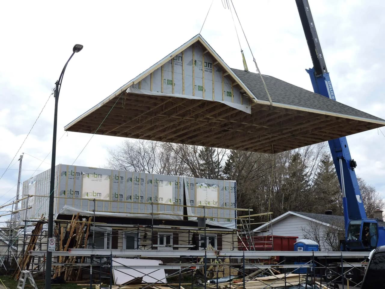 Prefabricated roof being lifted by a crane for installation on a residential home extension under construction.