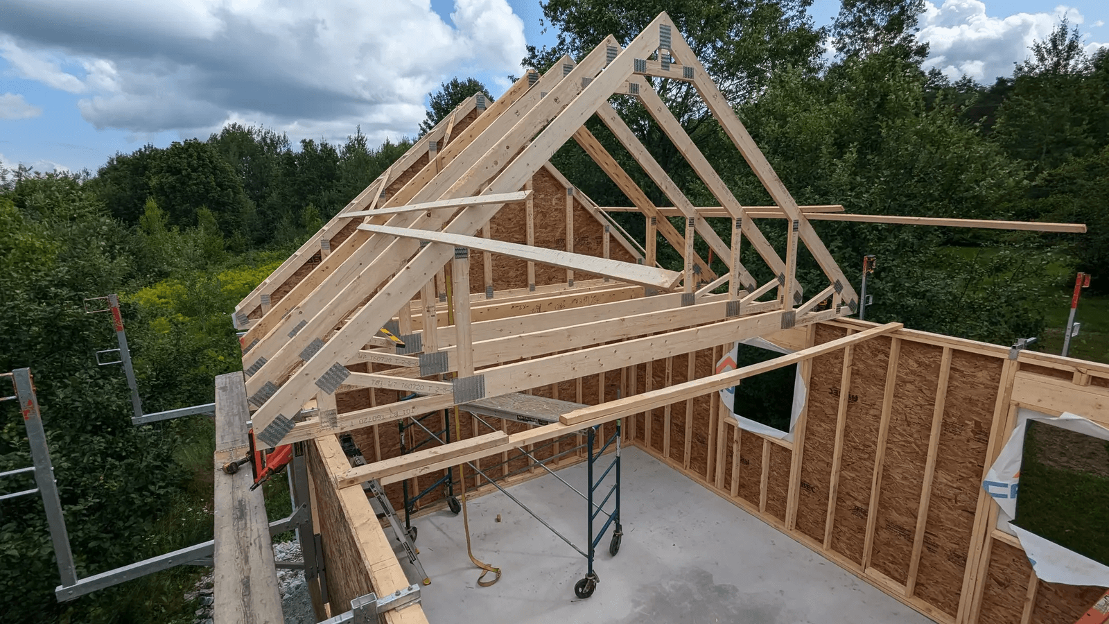 Wood framing of a house under construction with roof trusses, framed walls, structural sheathing and scaffolding on a residential job site