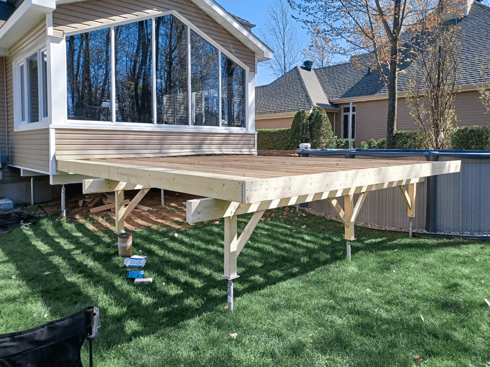 Wood deck structure under construction attached to a home with a glass sunroom and above-ground pool