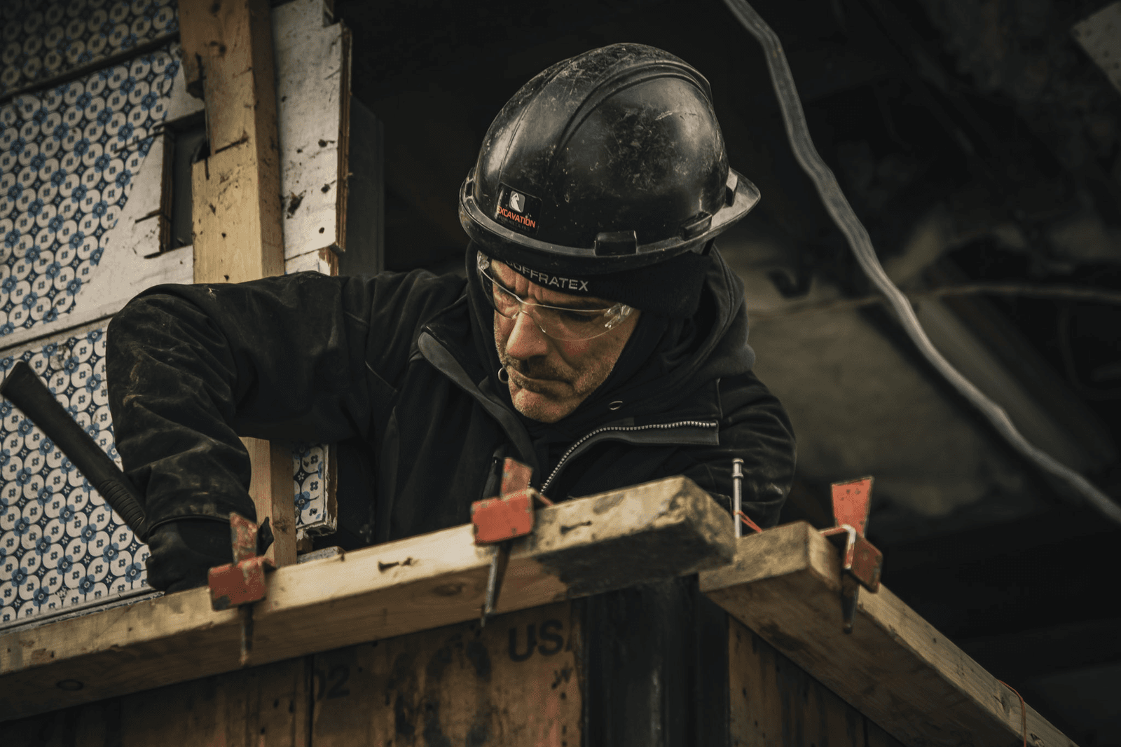 Construction worker wearing a hard hat and safety glasses performing wooden formwork on a renovation job site.
