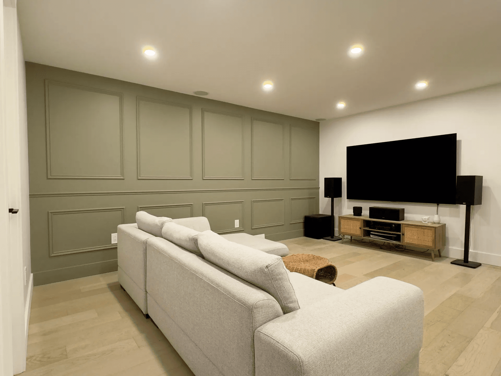 Modern living room with a green accent wall, a large gray sofa, a flat-screen TV, and an audio system.