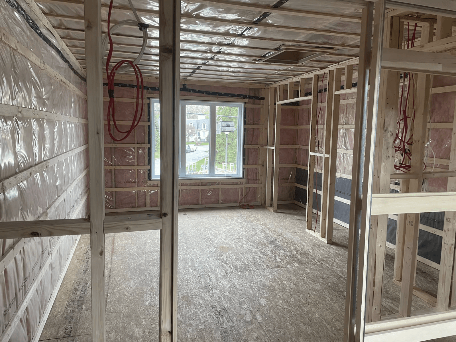 Residential room under construction with exposed wood framing, fiberglass insulation, vapor barrier, electrical wiring, and an installed window.
