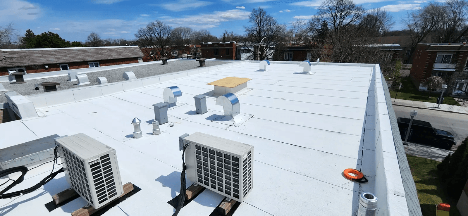 White flat roof of a residential building with air conditioning units, metal vents, and ventilation openings