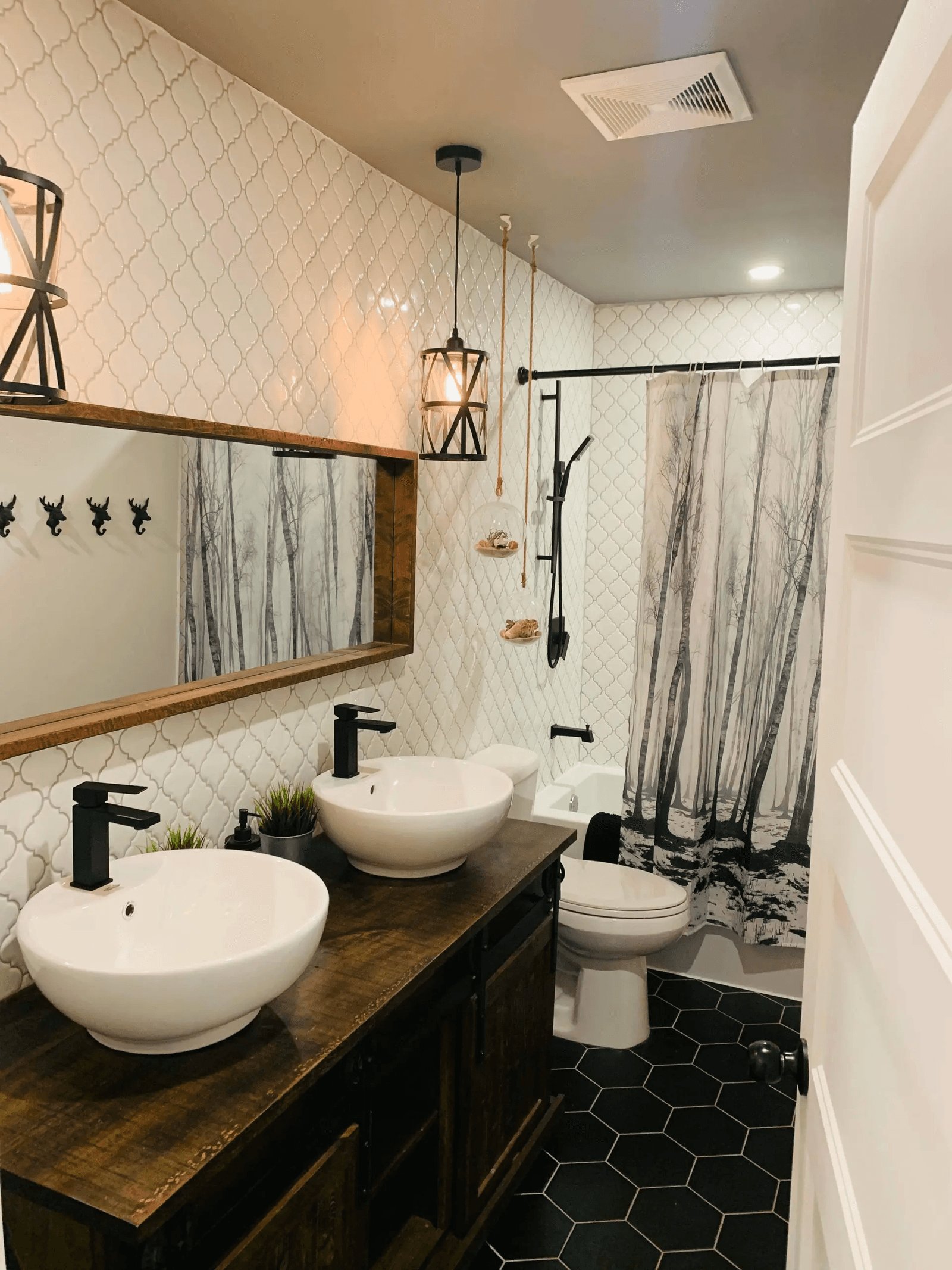 Renovated modern rustic bathroom featuring a double sink, dark wood vanity, patterned wall tiles and black hexagonal floor tiles.