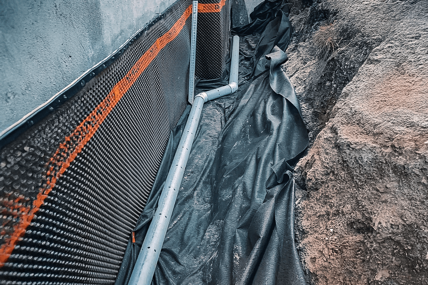Foundation drain installation with a waterproofing fabric against a house's foundation