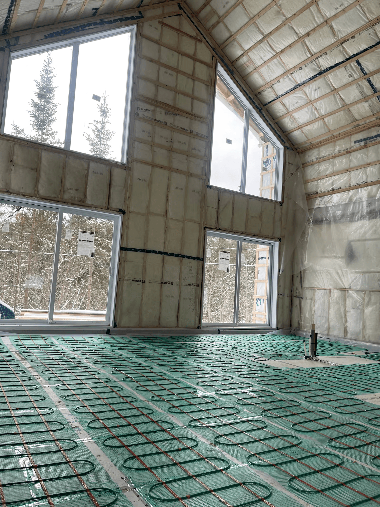  Large residential room under construction with radiant floor heating installed, insulated walls and ceiling, large windows and preparation for interior finishing