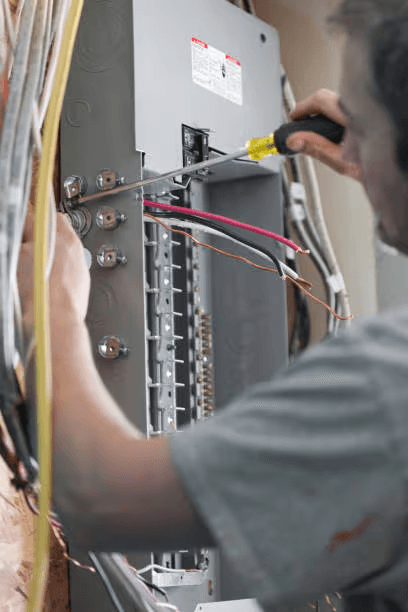 Electrician connecting and installing wiring inside an open residential electrical panel using a screwdriver