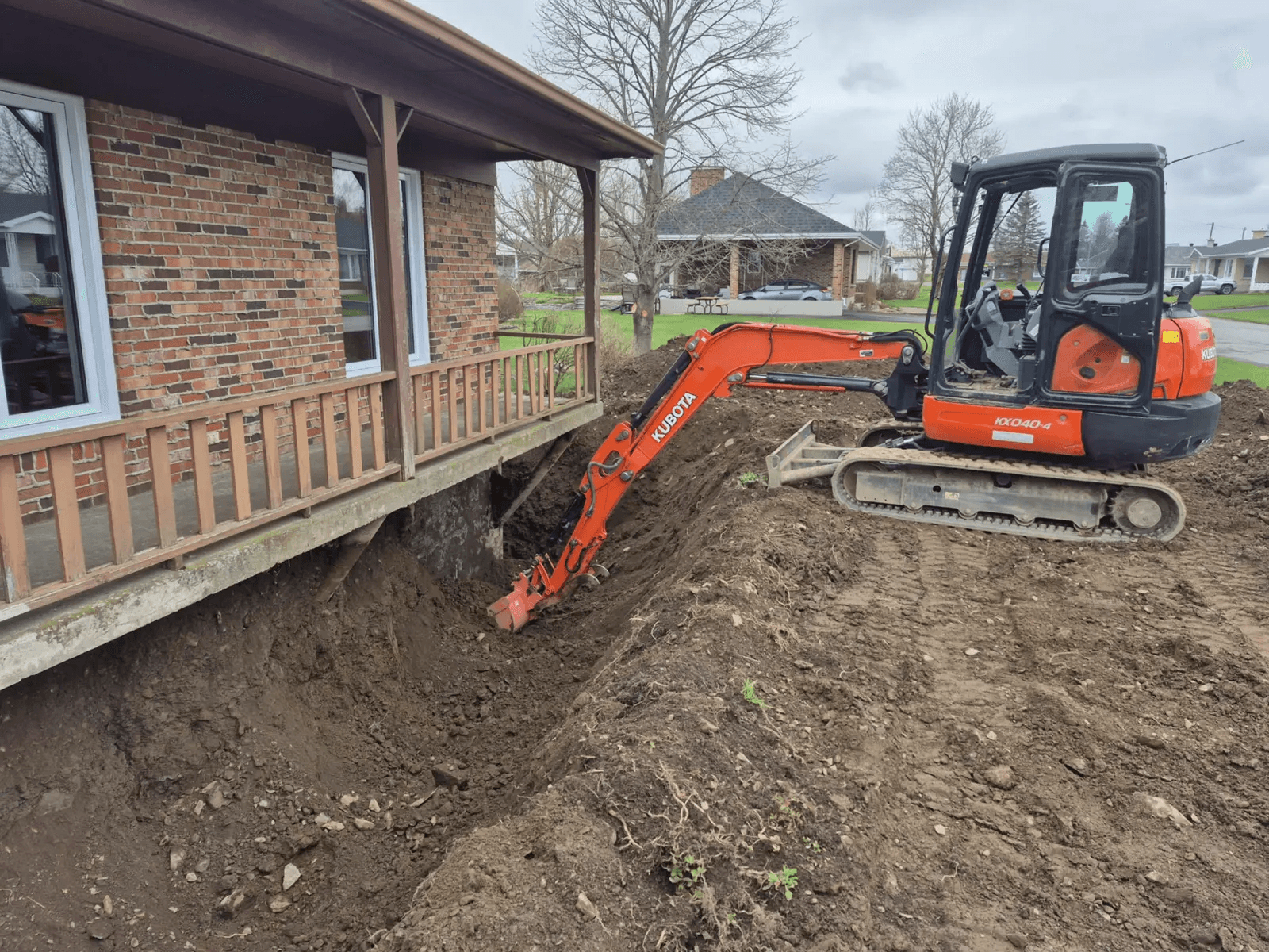 Excavation work with a mini excavator exposing the brick house foundation for waterproofing or French drain replacement.