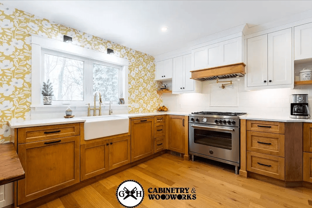 Rustic kitchen with wooden cabinets, yellow floral wallpaper, white farmhouse sink, white quartz countertops, and stainless steel stove.