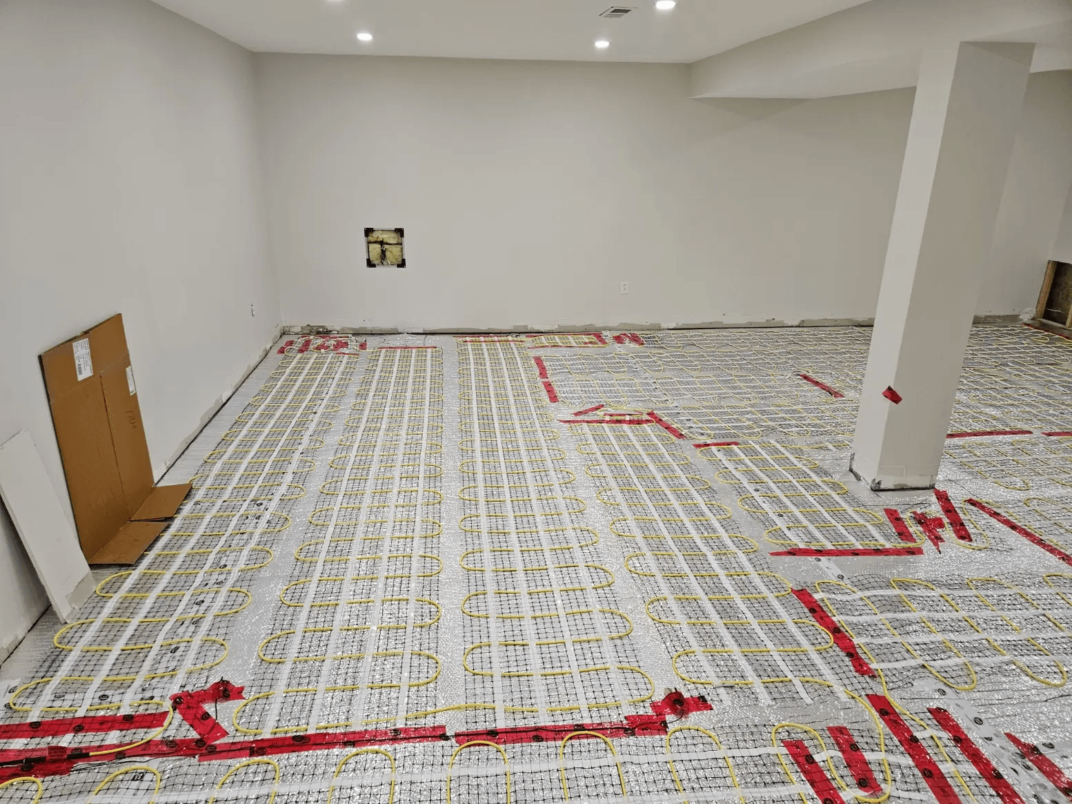 Electric radiant floor heating installation with yellow heating cables secured over an insulated membrane in a basement under renovation