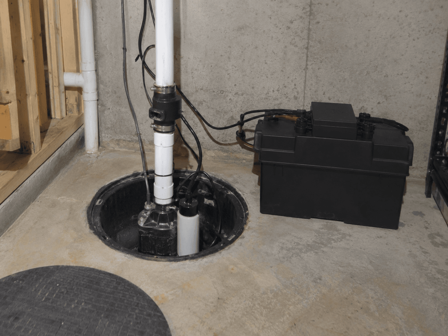 Sump pump system installed in a basement pit with PVC piping and a backup battery to help prevent water infiltration