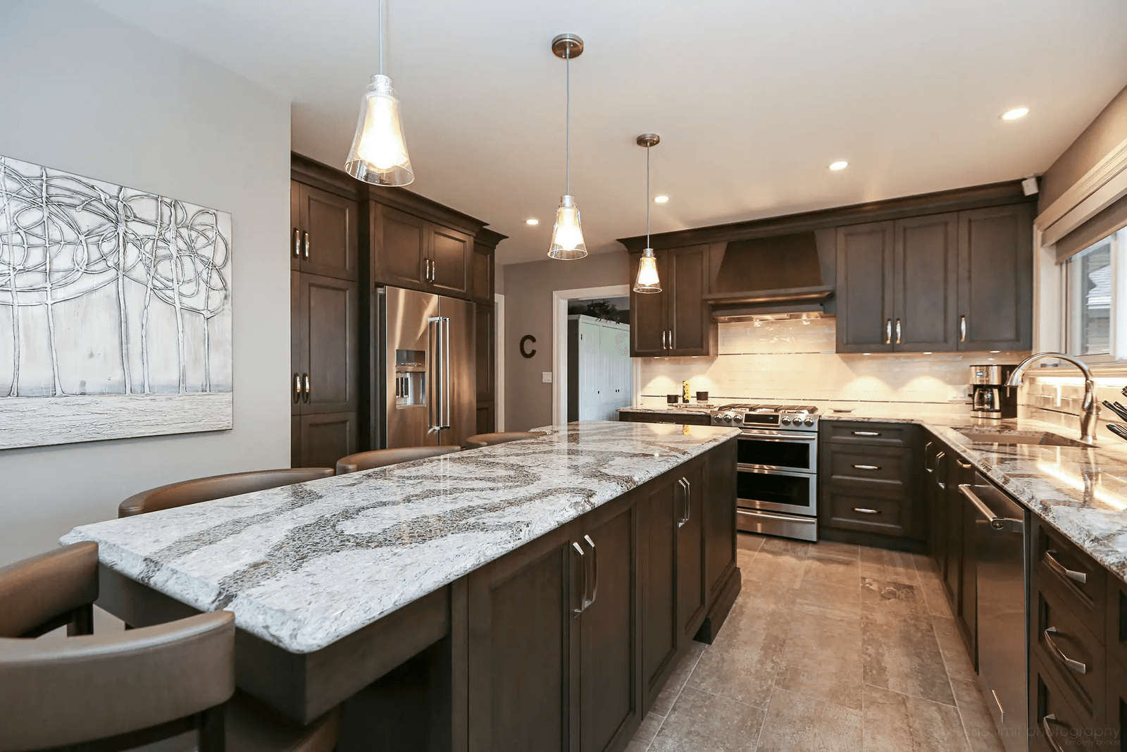 Traditional-style kitchen in Montreal featuring a spacious central island with a veined granite countertop. Dark wood cabinets and brushed nickel handles add elegance, while neutral ceramic flooring creates a balanced backdrop.