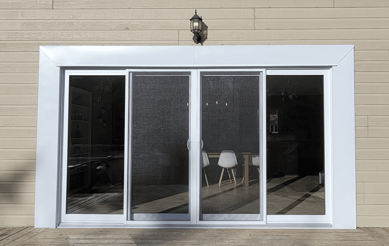 Large sliding glass patio door with white frame, central screen doors and beige horizontal exterior siding opening onto a wooden deck.