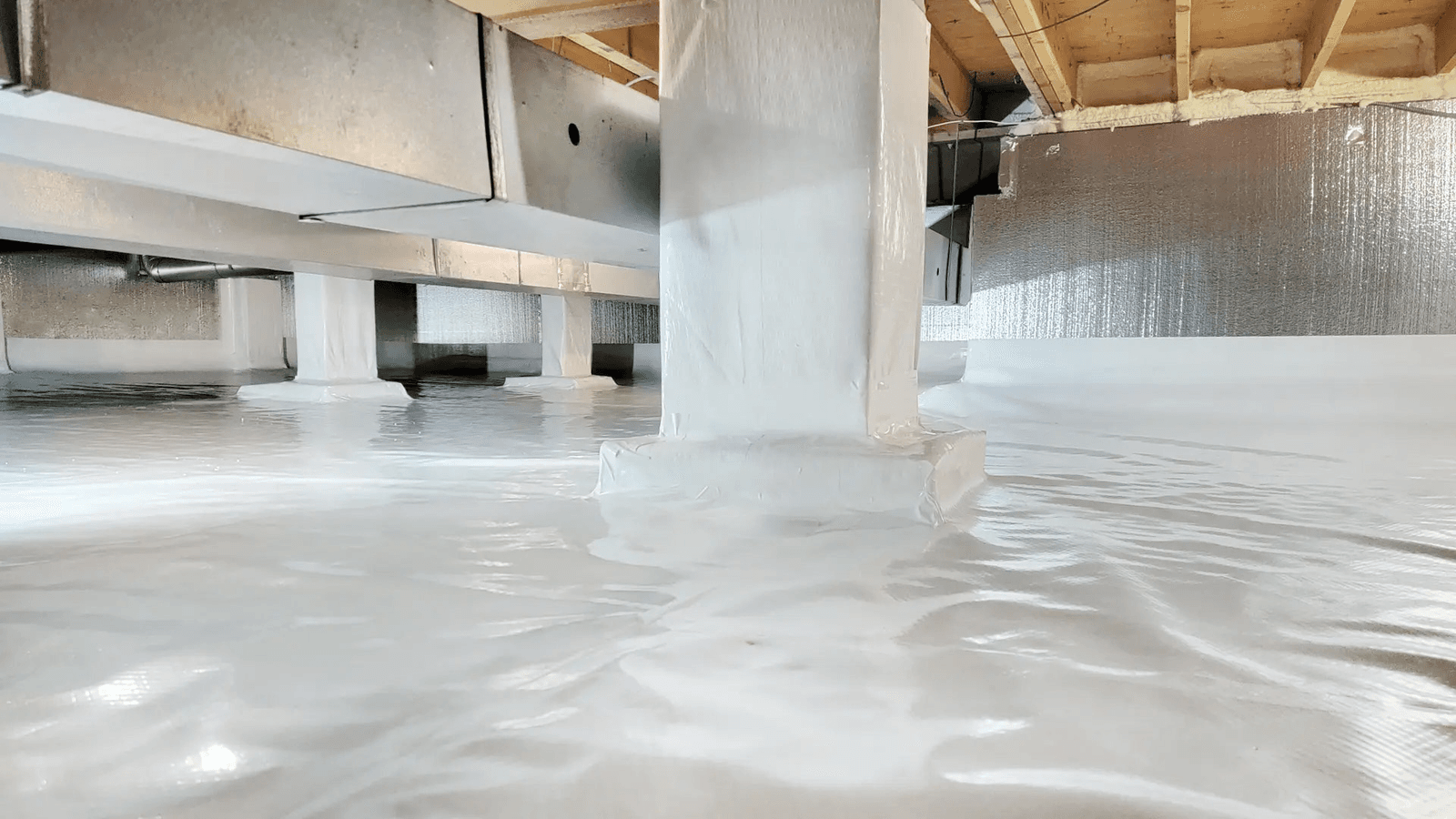 Insulated and sealed crawl space with a white vapour barrier covering the floor and support posts beneath a residential structure.