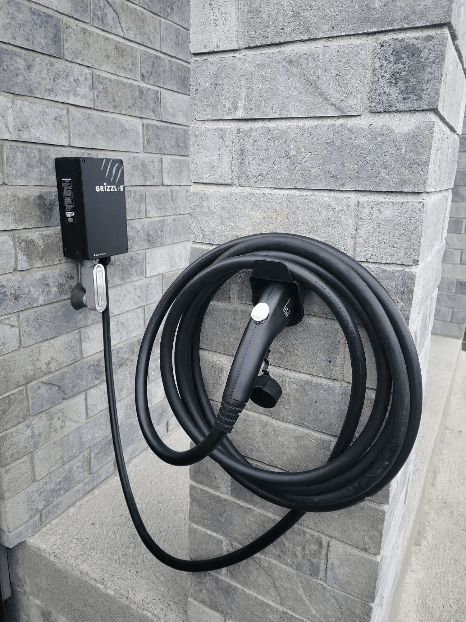 Residential electric vehicle charging station mounted on a brick wall with a coiled charging cable and wall-mounted connector