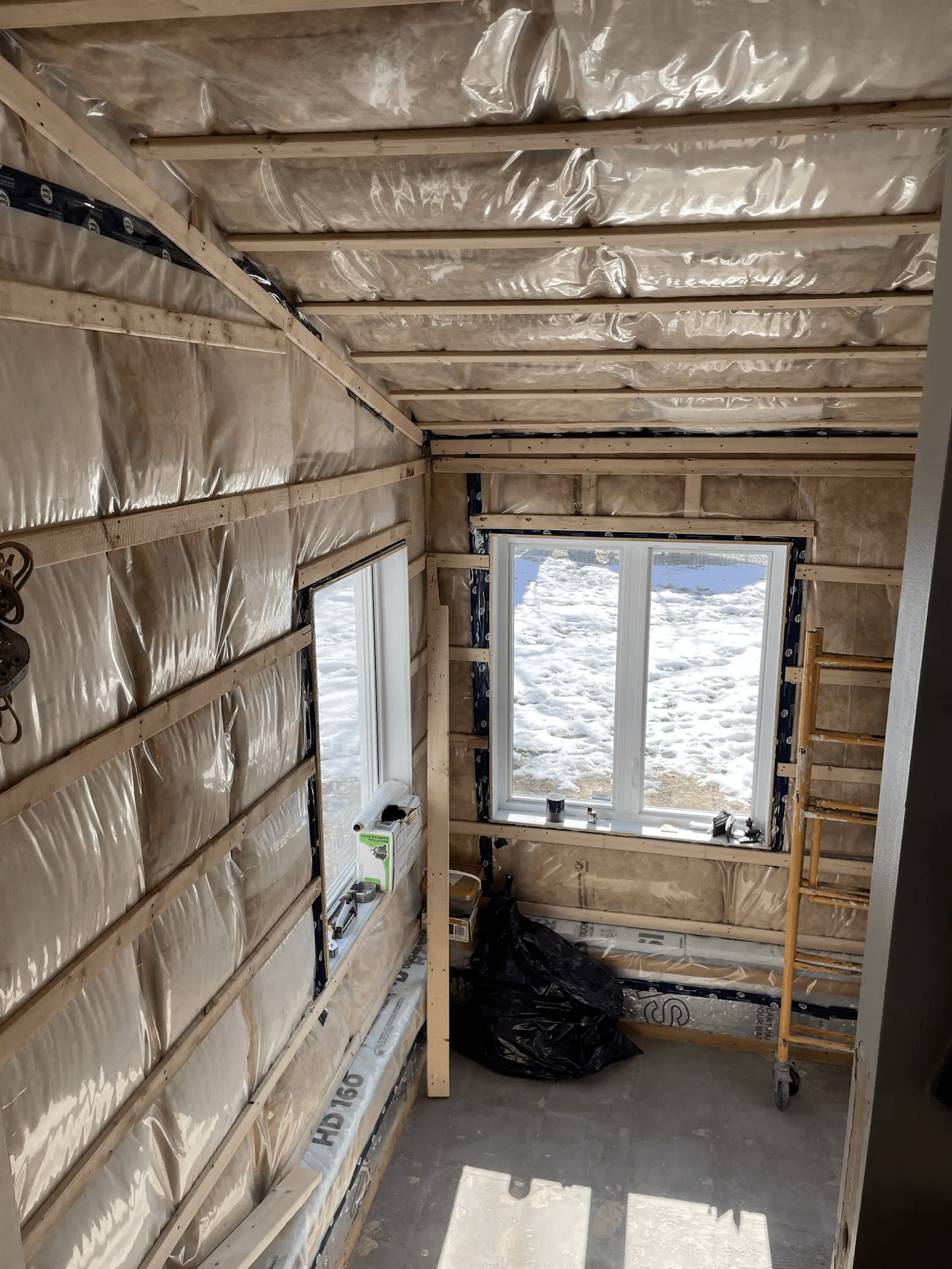 Room under renovation with insulated walls and ceiling, clear vapour barrier, exposed wood framing and installed windows.