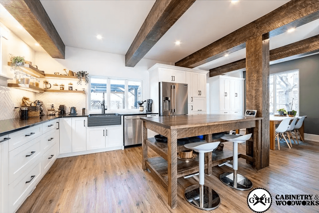 Modern kitchen with a solid wood central island, exposed beams, white cabinets, and recessed lighting. Open-concept kitchen leading to the dining area with large windows.