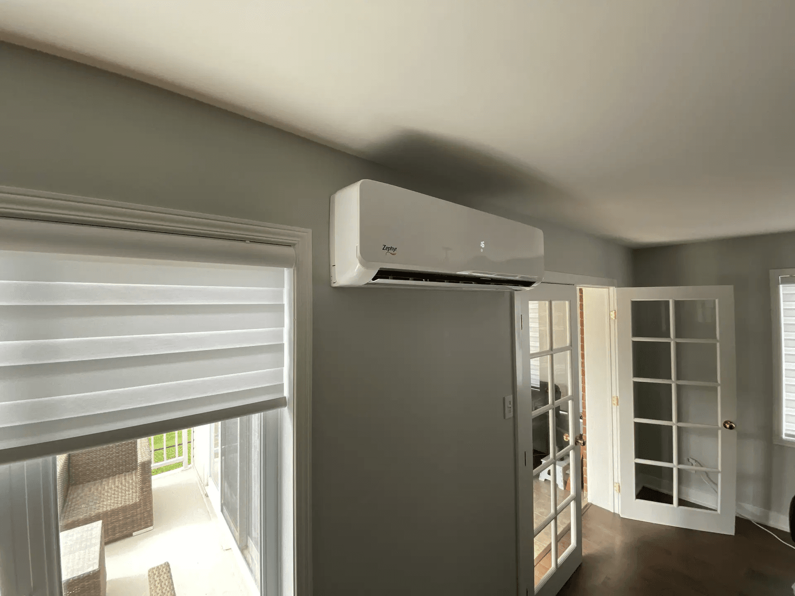 Zephyr wall-mounted air conditioning unit installed in a room with gray walls, a glass door, and a white blind.