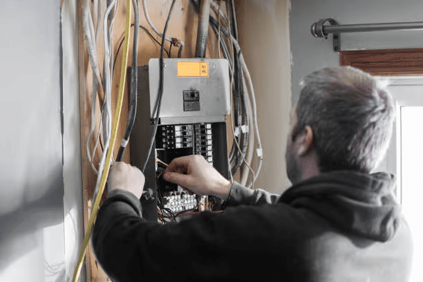 Electrician performing wiring work inside an open residential electrical panel with circuit breakers and visible wiring