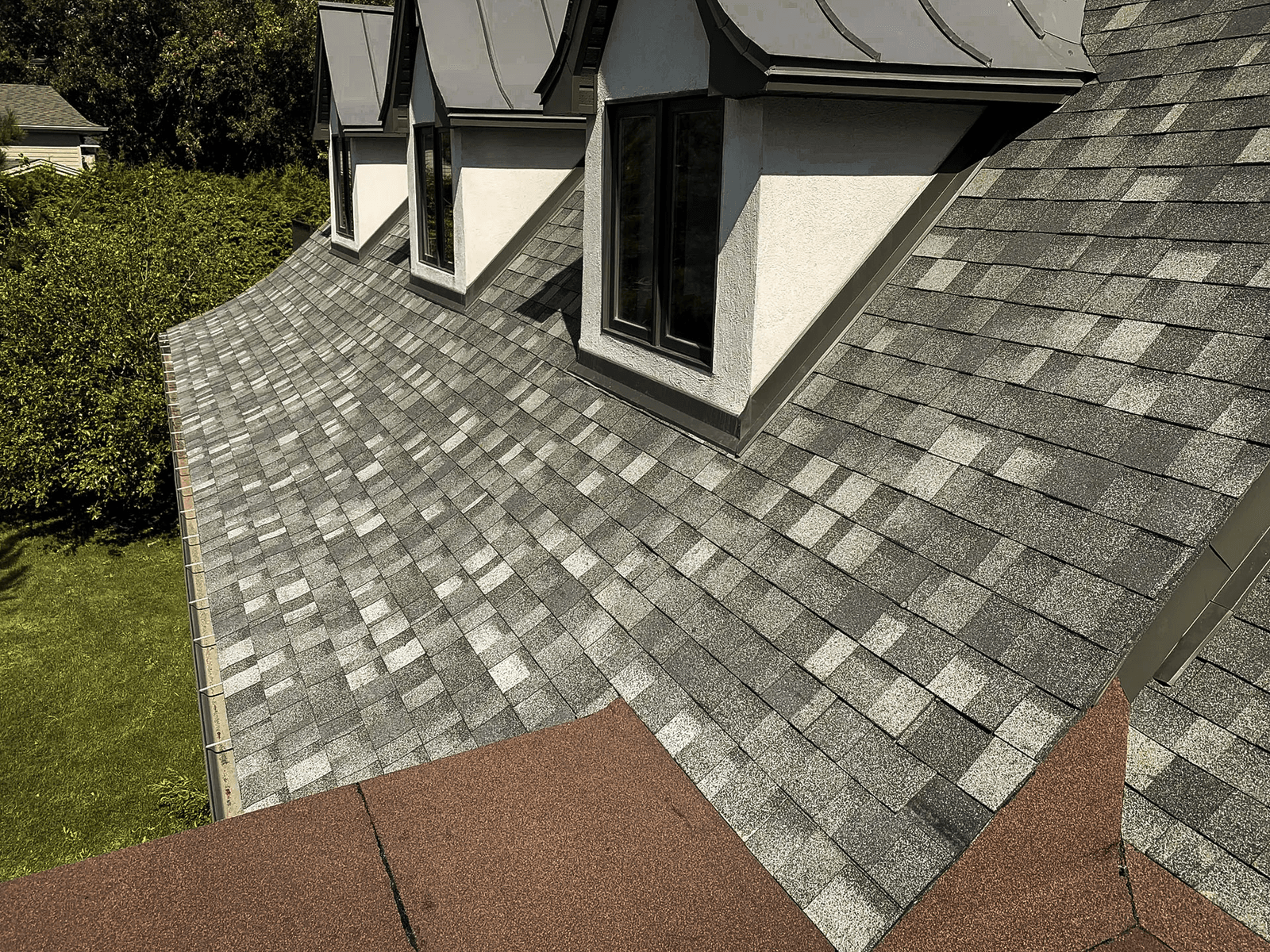 Residential roof with asphalt shingles and dormers overlooking a green garden.