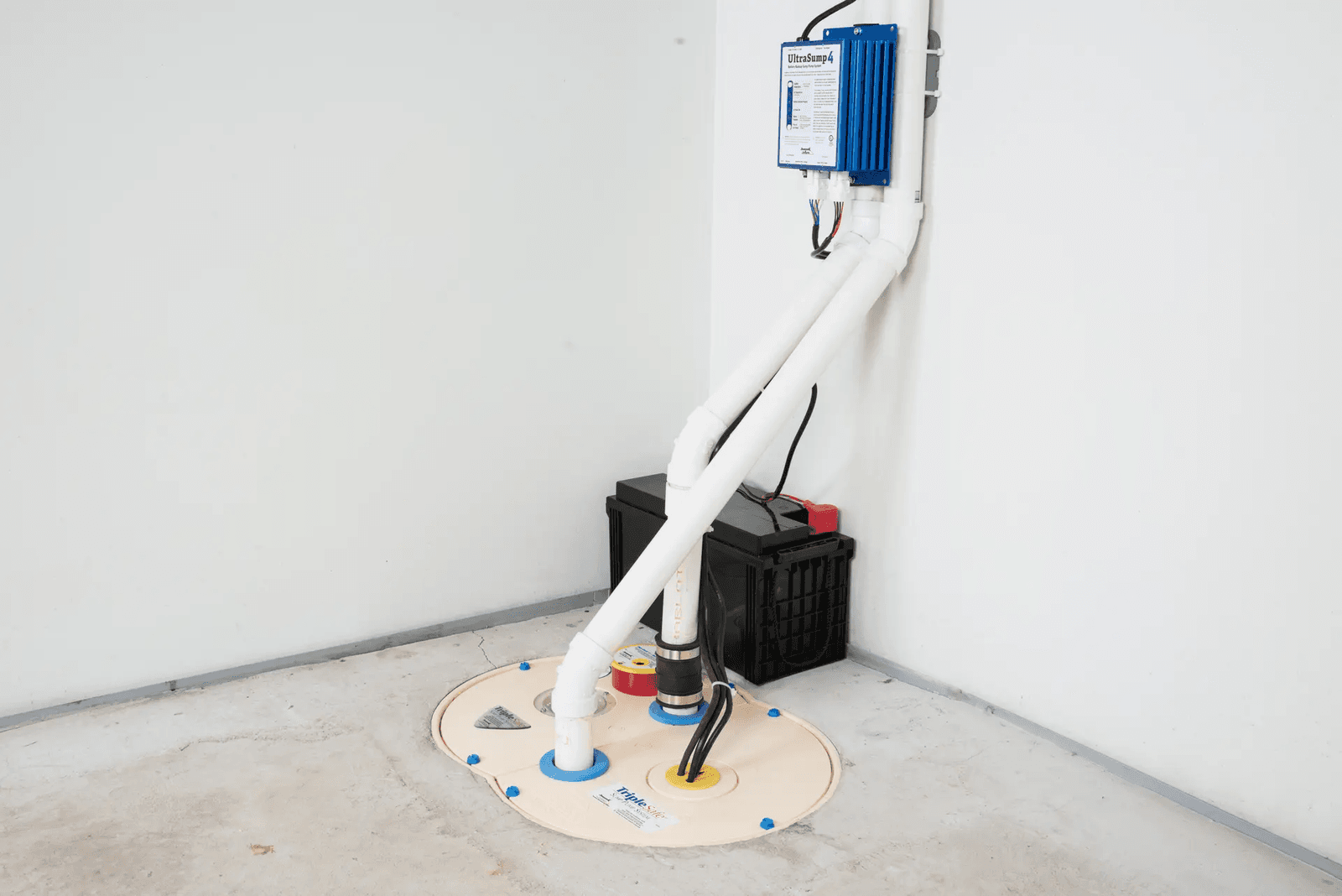 Sump pump system with a sealed cover, PVC piping, backup battery and wall-mounted controller installed in a basement