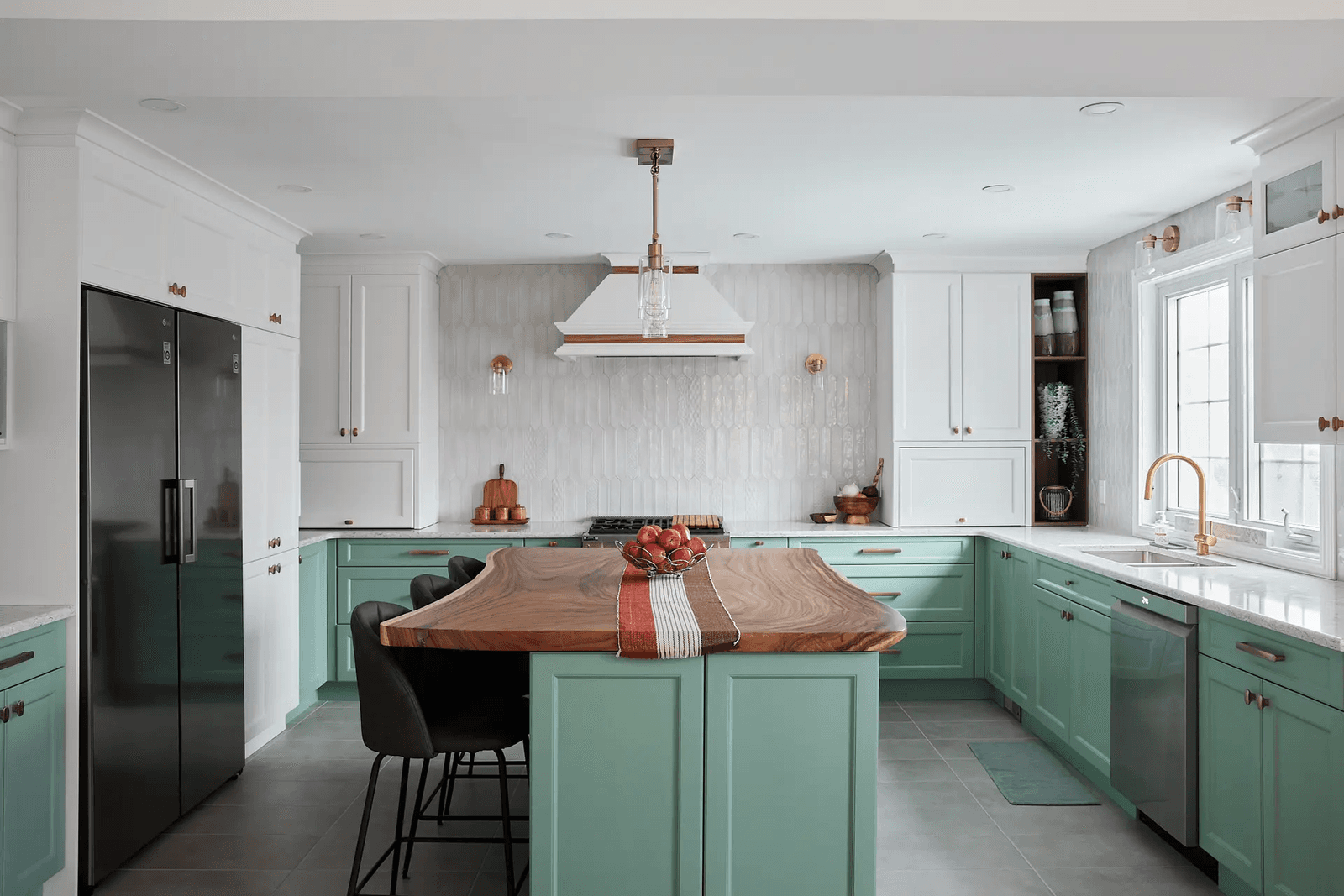 Transitional-style kitchen in Montreal featuring a natural wood veneer central island with clean lines. Mint green cabinets and copper handles add freshness and elegance, while the textured backsplash and neutral ceramic flooring create contrast.